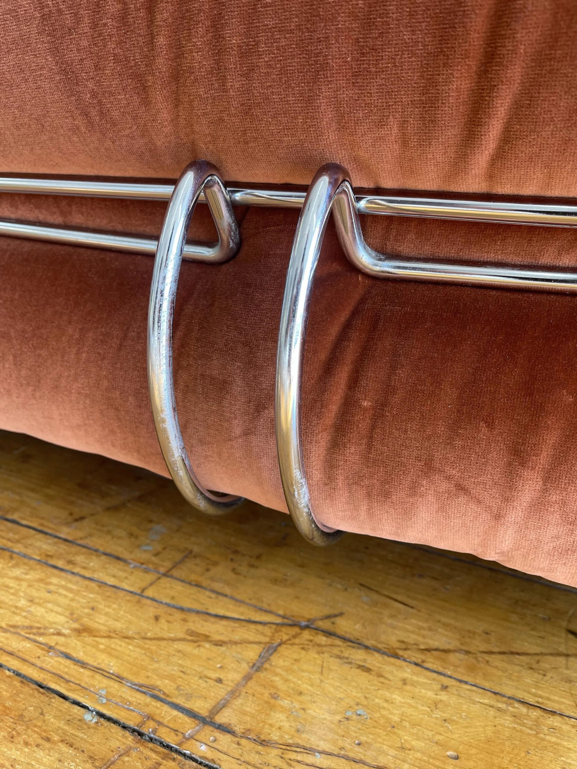 Close detail of the chrome clamp wrapping rust velvet upholstery on the Soriana